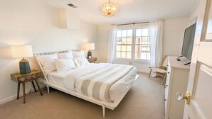 Une chambre à coucher avec un lit, deux tables de chevet avec des lampes, une télévision et une fenêtre avec des rideaux.