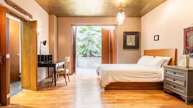 Une chambre à coucher avec un lit, un bureau et une commode. Une porte donne accès à une autre pièce.