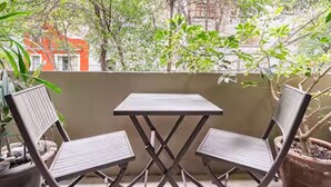 Un balcon avec deux chaises en métal et une petite table, entouré de plantes en pot et d’arbres.