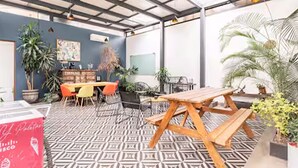 Un espace extérieur abrité, doté d’un sol à motifs, de tables et de chaises en bois, ainsi que de plantes en pot.