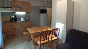 Eine kompakte Küche mit Holzausstattung, einem Esstisch mit Stühlen, einer Mikrowelle, einem Kühlschrank und einem dunkelgrauen Sofa.