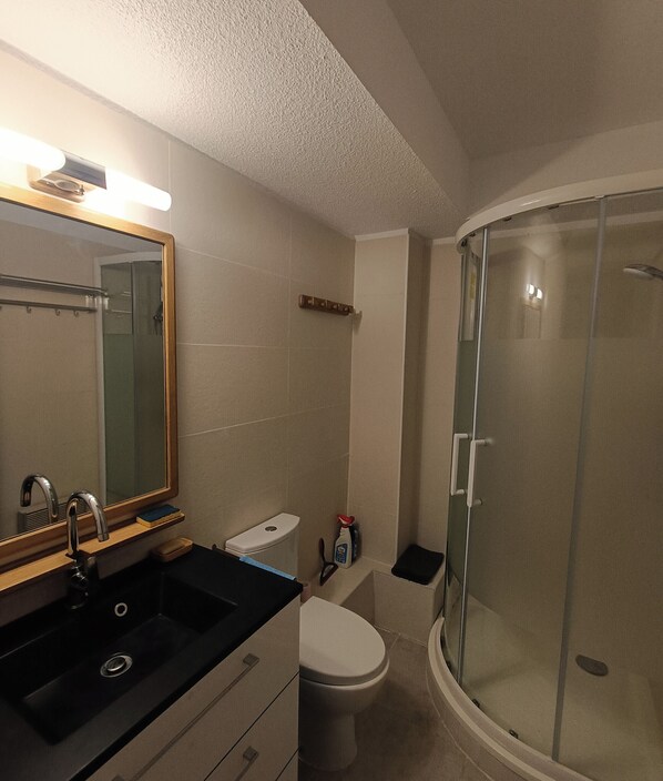 A bathroom with a sink, mirror, toilet, and a glass-enclosed shower.