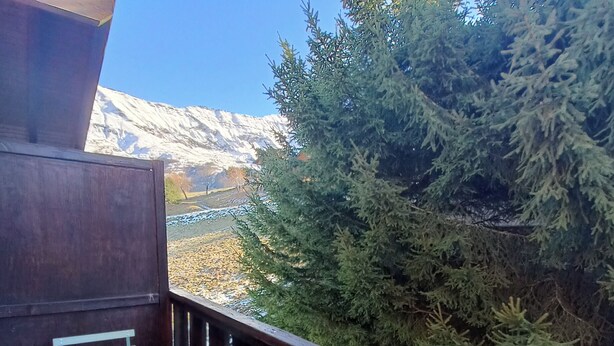Ein Balkon mit Tisch und Stühlen, einem Holgitter und Blick auf schneebedeckte Berge und immergrüne Bäume.
