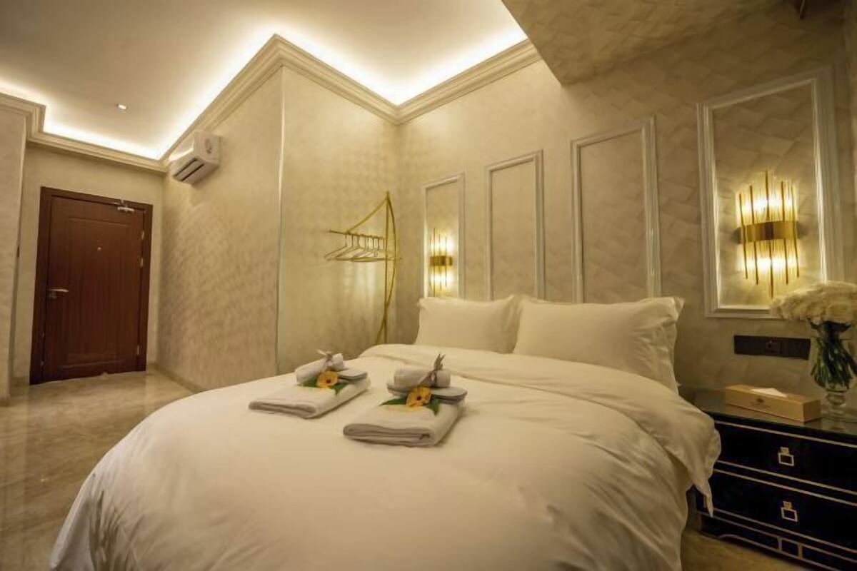 A hotel room with a large bed, a dresser, a mirror, and a wall-mounted light fixture.