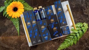A tray of skincare products with blue packaging and gold accents, arranged on a marble surface with green leaves and a sunflower. - A Residence - A Member of The Luxury Stay Group (Kota Kinabalu)