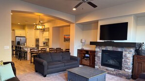 A living room with a fireplace, a television mounted above it, and a dining area in the background.