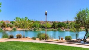 A well-maintained lawn with a lamp post, a clear blue sky, and a lake with surrounding greenery.