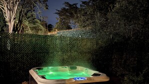Un bain à remous dans un espace jardin, avec une terrasse en bois et une haie en arrière-plan.