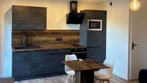 Une cuisine moderne avec des meubles de couleur sombre, un plan de travail en bois et un coin repas comprenant une table et des chaises.