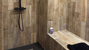 Un espace douche avec un mur en bois, un banc et une petite étagère sur laquelle se trouve une bouteille.