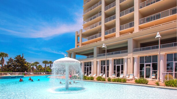 A hotel with a large pool featuring a central fountain, multiple balconies, and a clear blue sky. - Life is Better at the Beach!  Charming 3 bedroom, 3 bath condo at Ariel Dunes 1 (Miramar Beach)
