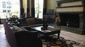 A living room with a dark-colored sofa set, a glass coffee table, and a patterned rug. There is a fireplace with a mantel and a television on a stand. - Pool View 2 Bedroom/2 Bath Condo in Houston's Medical Center (Houston)