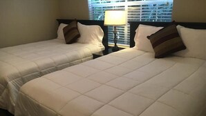Two beds with white bedding and dark headboards, a bedside table with a lamp, and a window with blinds. - Pool View 2 Bedroom/2 Bath Condo in Houston's Medical Center (Houston)