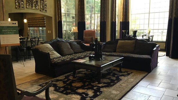 A spacious living room with a large sectional sofa, a coffee table, and a patterned rug. There are large windows with curtains, a fireplace, and a dining area in the background. - Pool View 2 Bedroom/2 Bath Condo in Houston's Medical Center (Houston)
