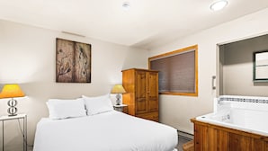 Hotellihuone, jossa on suuri sänky, puinen vaatekaappi, kylpyammeella varustettu kylpyhuone ja taulu seinällä.