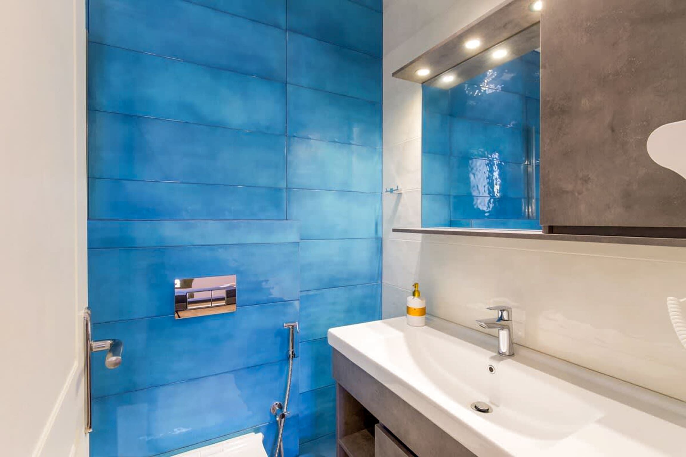 Ein Badezimmer mit blauen Fliesen, einem weißen Waschbecken und einem Spiegel.