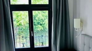 Une chambre avec une grande fenêtre, un lit et une table de chevet.