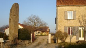A rustic stone house with a dirt path leading to the entrance, surrounded by greenery and a tall stone structure. - Chalet du Menhir - SAINT-MICAUD (SAINT-MICAUD)