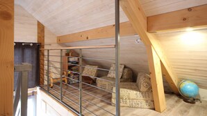 A loft bedroom with a sloped ceiling, a metal railing, a bed with patterned bedding, a globe, and a shelf with books and a plant. - Chalet du Menhir - SAINT-MICAUD (SAINT-MICAUD)