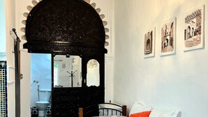 A bedroom with a black and white checkered floor, a bed with a floral bedspread, a wooden headboard, a black arched doorway, and a chandelier. - Riad Nostalgie (Tetouan)