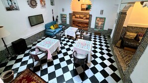 A room with a checkered floor, a sofa, two tables with chairs, a TV, and decorative wall art. - Riad Nostalgie (Tetouan)