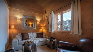 A cozy cabin interior with a wooden interior, a sofa, a leather armchair, a small table, and a window with curtains. - Chalet San Marco - mountain luxury stay for 6 - OVO Network (La Clusaz)