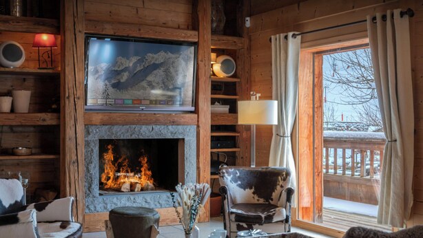 A cozy cabin interior with a fireplace, wooden furniture, and a view of a snowy landscape. - Chalet San Marco - mountain luxury stay for 6 - OVO Network (La Clusaz)