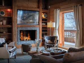 A cozy cabin interior with a fireplace, wooden furniture, and a view of a snowy landscape. - Chalet San Marco - mountain luxury stay for 6 - OVO Network (La Clusaz)