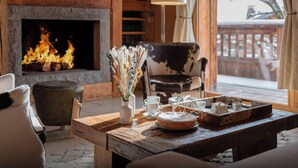 A cozy living room with a fireplace, a wooden table with a cake, and a cowhide chair. - Chalet San Marco - mountain luxury stay for 6 - OVO Network (La Clusaz)
