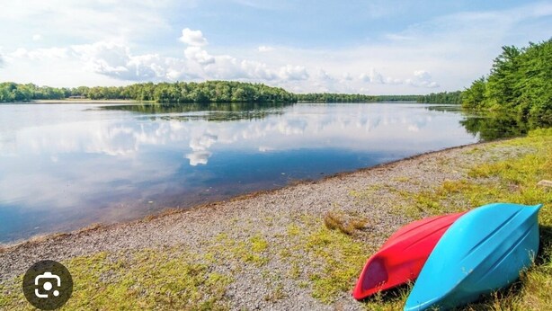 A calm lake with a clear reflection, a grassy shore, and a red and blue kayak.