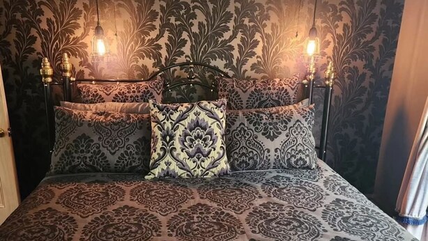 Una cama con una colcha estampada y dos almohadas a juego, un cabecero con un diseño decorativo y dos lámparas fijadas a la pared.