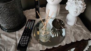 Un control remoto, un jarrón decorativo, un candelabro y un pequeño recipiente de vidrio sobre una mesa con mantel de encaje.