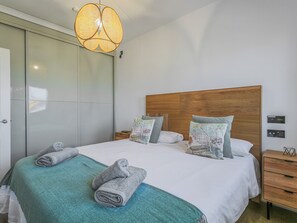 A neatly made bed with a teal blanket, two pillows with floral patterns, and two rolled towels on the bed.