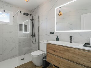 A modern bathroom with a glass-enclosed shower, a white toilet, a wooden vanity with a mirror, and a marble-tiled wall.