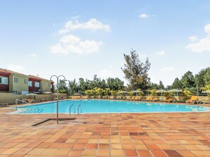 A swimming pool with tiled flooring, sun loungers, and umbrellas.