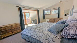 Een slaapkamer met een groot bed, een houten dressoir, een stoel en uitzicht op de omgeving via een schuifdeur.