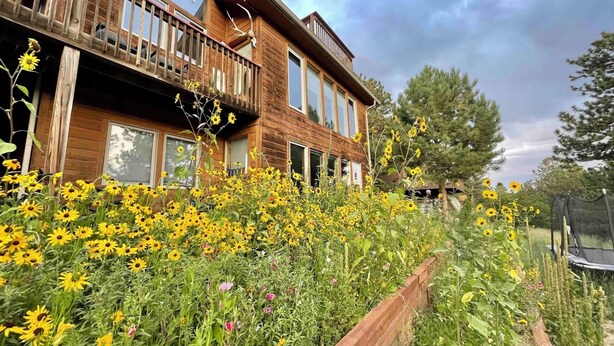 Een houten huis met balkon, omgeven door een tuin vol diverse bloemen.