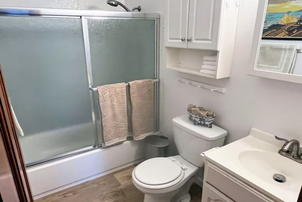A bathroom with a glass-enclosed shower, a toilet, a sink, and a cabinet with towels.