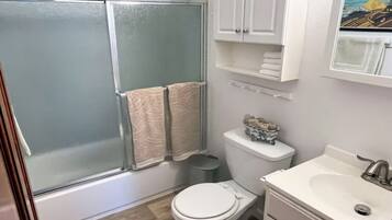 A bathroom with a glass-enclosed shower, a toilet, a sink, and a cabinet with towels.