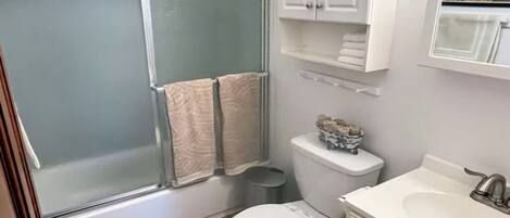 Et badeværelse med bruseniche, toilet, vask og et skab med håndklæder.