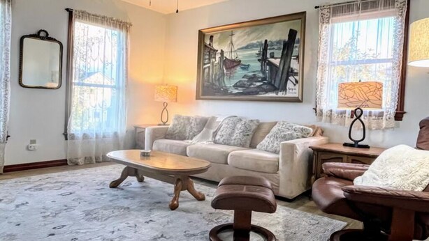 Un salon avec un canapé, une table basse et un fauteuil. Il y a un tableau au mur et deux lampes de chaque côté.