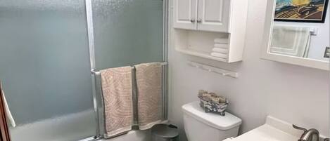A bathroom with a glass-enclosed shower, a toilet, a sink, and a towel rack.