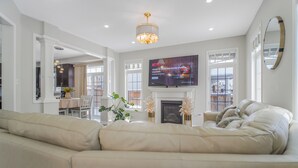 A modern living room with a large beige sectional sofa, a fireplace, and a flat-screen TV mounted above it.