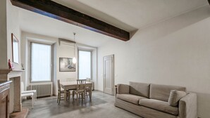 Un salon spacieux avec une grande fenêtre, un coin repas avec une table et des chaises, et un canapé beige.