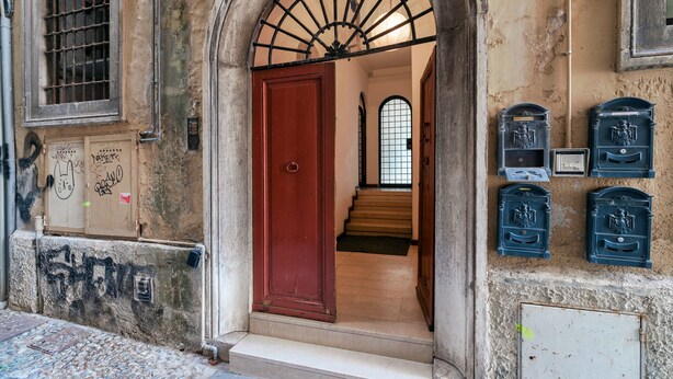 Une entrée en arc surmontée d’une porte rouge, un escalier menant à l’intérieur et des boîtes aux lettres fixées au mur.
