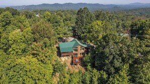 A lodge with a green roof, surrounded by dense forest and mountains in the background. - Views, Hot tub, Pool Table! (Sevierville)