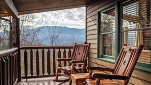 A wooden porch with a view of mountains, wooden rocking chairs, and a window with blinds. - Views, Hot tub, Pool Table! (Sevierville)