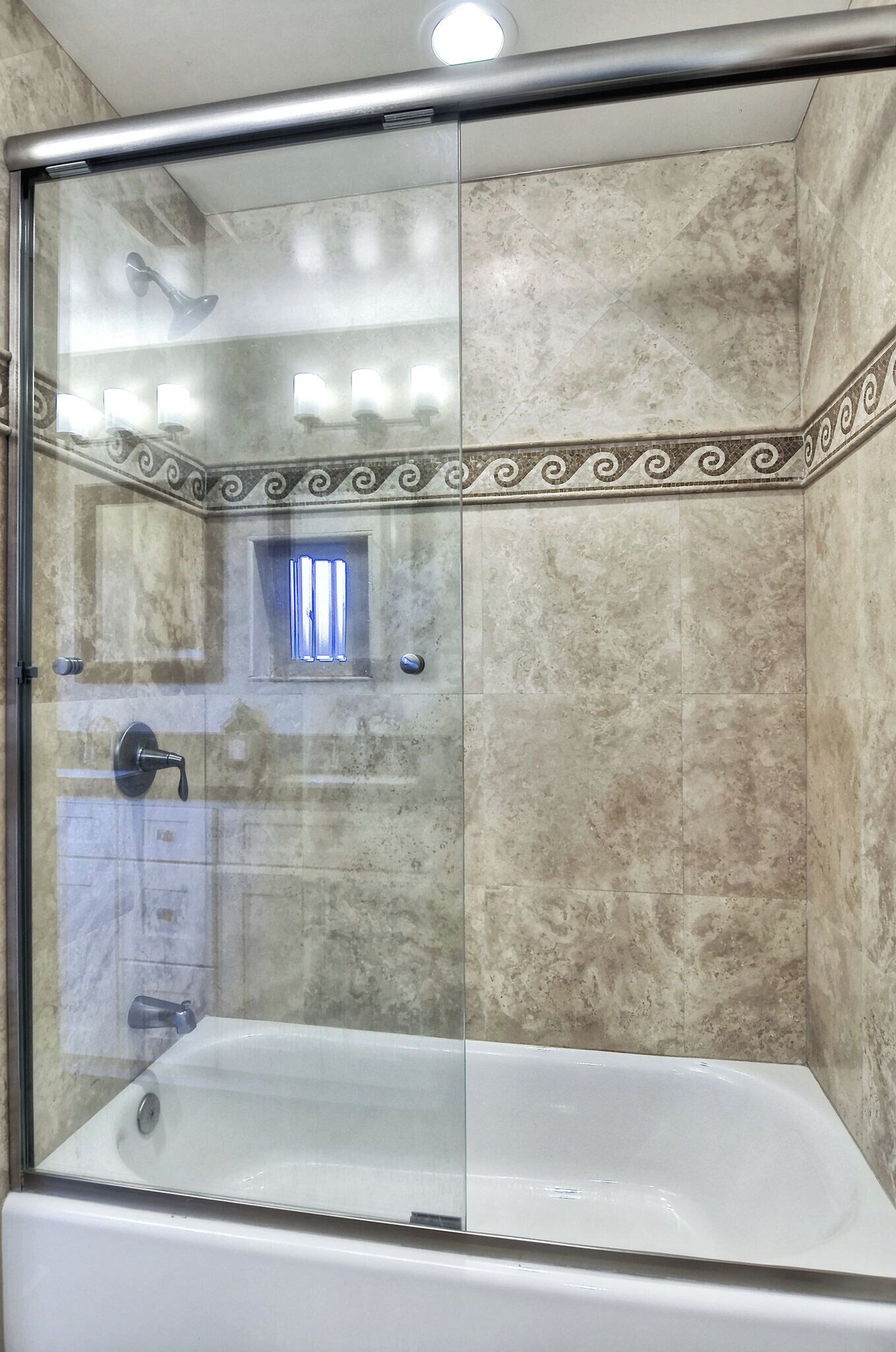 Ein Duschbereich mit Glasabtrennung, einer Badewanne, Marmorfliesen und einer dekorativen Bordüre.