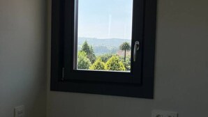 Une pièce dotée d’une fenêtre donnant sur un paysage arboré, avec un bâtiment visible au loin.