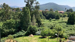 Un jardin luxuriant, avec différents arbres et arbustes, une zone délimitée par une clôture et, au fond, un bâtiment doté d’un toit rouge.